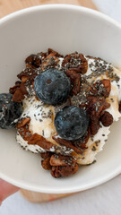 Delicious blueberry yogurt bowl with granola and chia seeds in white dish - healthy breakfast concept of cafes, health food stores, fitness centers