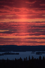 Sunset colours in the clouded sky over forested lake landscape in winter in Finland