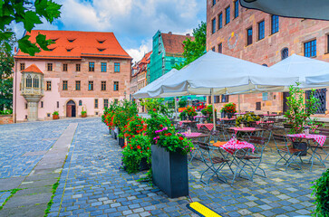 Street restaurant outdoor cafe with tables and chairs in empty square Sebalder Platz in summer day, medieval buildings in Old town Nuremberg city historical center, Middle Franconia region, Germany