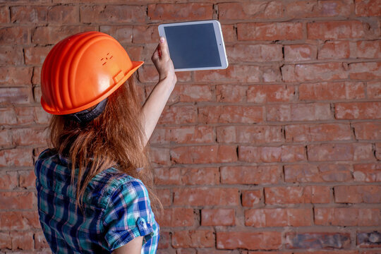 A woman in an orange hard hat holding a tablet computer