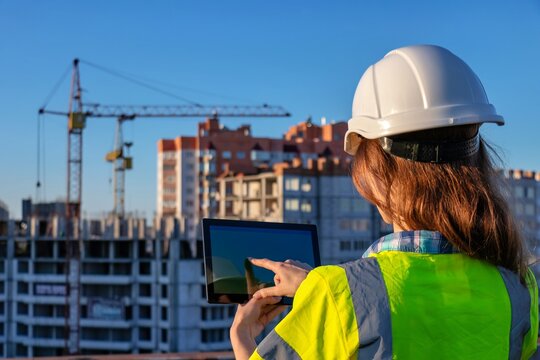 A woman in a hard hat and safety vest using a tablet computer