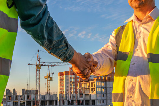 Two construction workers shaking hands in front of a construction site