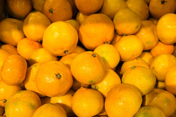 vibrant pile ripe mandarins glowing in warm light, market crate closeup showcasing dewy skin, scattered stems, glossy texture, vivid orange color, harvest abundance and commercial freshness ready for