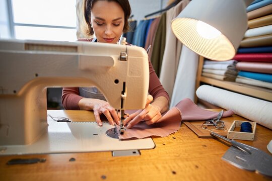 Sewing studio scene focused woman at machine beside fabric bolts and thread.
