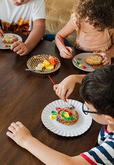 Kids decorating a large round cookie with edible paints and brushes during a tropical Christmas creative activity, painting festive designs like trees and ornaments, fun DIY holiday food art workshop