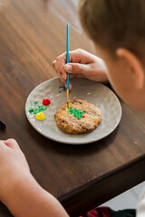 Kids decorating a large round cookie with edible paints and brushes during a tropical Christmas creative activity, painting festive designs like trees and ornaments, fun DIY holiday food art workshop