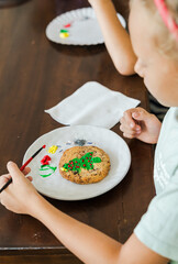 Kids decorating a large round cookie with edible paints and brushes during a tropical Christmas creative activity, painting festive designs like trees and ornaments, fun DIY holiday food art workshop