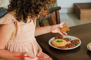 Kids decorating a large round cookie with edible paints and brushes during a tropical Christmas creative activity, painting festive designs like trees and ornaments, fun DIY holiday food art workshop