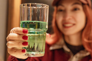 Woman holding a glass of bright green tarragon soda at the table in a cozy restaurant