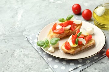 Tasty bruschettas with mozzarella cheese, tomatoes and basil on grey textured table, closeup. Space for text