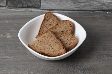 Slices of whole grain bread in a white bowl on a wooden surface ready for a healthy meal or snack