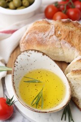 Tasty baguette served with oil, tomatoes and rosemary on white marble table, closeup
