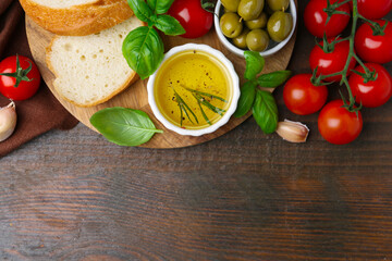 Tasty baguette served with oil, tomatoes, olives and basil on wooden table, flat lay. Space for text
