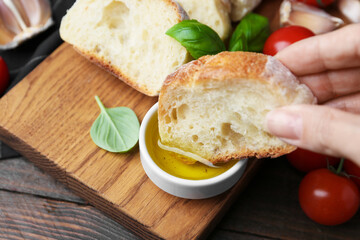 Woman dipping piece of baguette into oil at wooden table, closeup