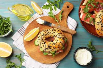 Delicious bagels with salmon, cream cheese, cucumber, arugula and lemon on light blue wooden table, flat lay