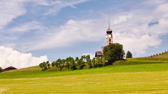St. Valentin church surrounded green lush fields on sky background, in Dolomites Alpe di Suisi. South Tyrol, Italy