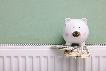 Piggy bank and dollar banknotes on heating radiator near green wall, closeup