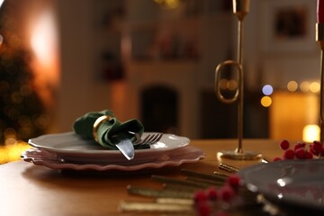 Christmas table setting with plates and cutlery in festive decorated room, closeup