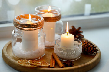 DIY Christmas lanterns. Burning candles in glass jars, cones and spices on window sill indoors, closeup