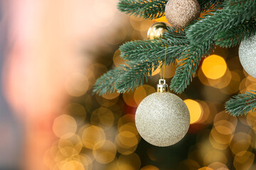 Christmas bauble hanging on fir tree branch against blurred lights, closeup with space for text. Bokeh effect