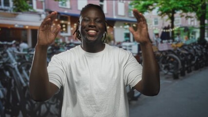 Man smiling with hands raised palms visible at street bike parking, wearing white t shirt and dreadlocks; joyful confidence. - Powered by Adobe