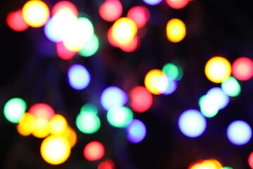 Obraz premium Blurred view of bright Christmas lights on dark background, bokeh effect