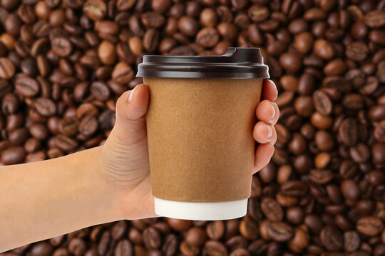 Woman holding takeaway paper cup, closeup. Roasted coffee beans on background