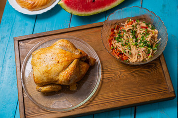 Couscous with dried fruits and turmeric, baked whole chicken, flatbread, and vegetable salad on a wooden table