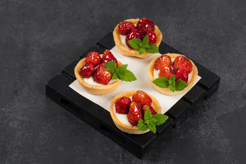 Vegan Mini dessert. Mini Round Vegan Strawberry tartlets. On a wooden board.  Dark background. Close up	