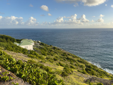 Coastal landscape at Pointe Milou in Saint Barth&eacute;lemy, with lush green hillside vegetation, ocean cliffs, and a wide view of the Caribbean Sea under a bright blue sky with scattered clouds. Peaceful i