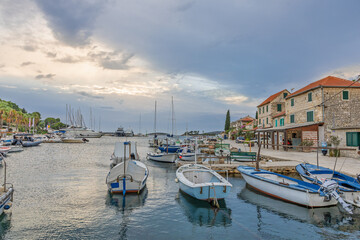 Calm Coastal Harbor With Boats and Waterfront Village Under Cloudy Blue Sky, Maslinica, Croatia