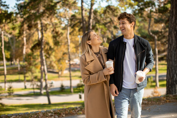 Fototapeta premium Couple enjoys a sunny walk in the park with coffee in the autumn breeze