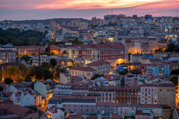 Illuminated buildings and rooftops of Lisbon, Portugal in afternoon twilight from Miradouro da Senhora do Monte overlook..