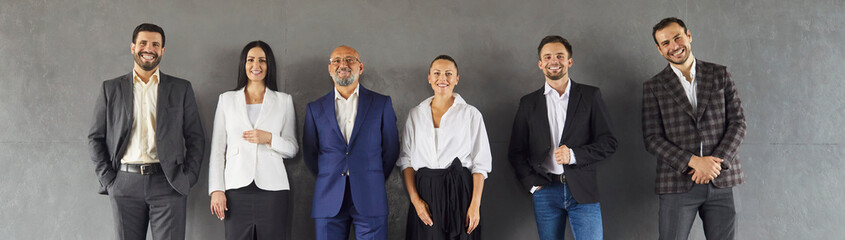 Group portrait of happy confident professional business people team standing in row by studio wall....