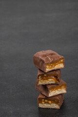 Chocolate bar with nougat, caramel, peanuts and hazelnuts. Dark background. Copy space