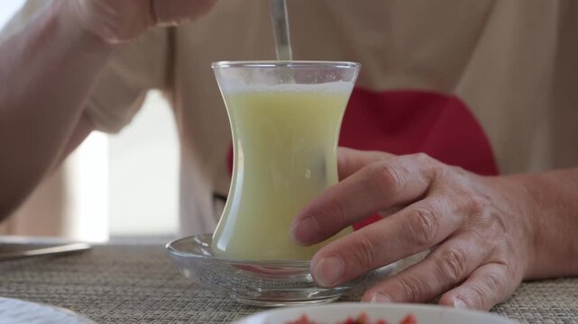 Woman hand stirring hot fruit drink in Turkish glass cup with teaspoon while sitting at table in cafe close-up
