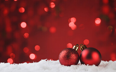 Two red christmas ornaments resting on white snow with a blurred red bokeh background