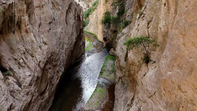 Sunlight reflecting on a stream flowing through a deep and narrow gorge. The rugged rock formations create a dramatic and wild landscape