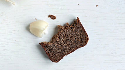 Bitten Dark rye bread slice and garlic clove on white wooden surface. End of meal. Half-eaten bread and garlic. Perfect for culinary inspiration, healthy eating for recipe blogs, cookbooks