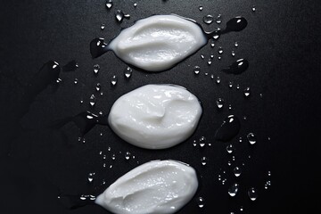 Three blobs of white cream surrounded by water droplets on black.
