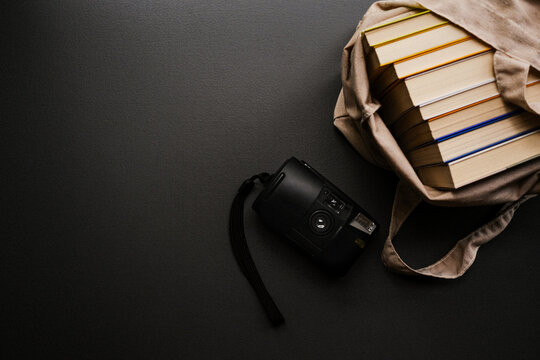 câmera analógica ao lado de livros enfileirados sobre fundo escuro com espaço livre para texto - Powered by Adobe
