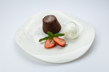 Chocolate lava cake with vanilla ice cream and strawberries on white plate, top view