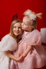 two little girls in elegant white dresses on a red background in a studio with gift boxes catching confetti for the New Year