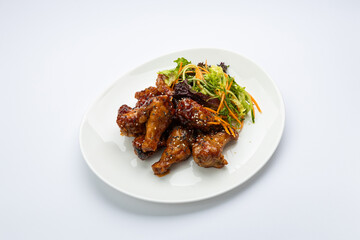 Glazed chicken wings with sesame and fresh slaw on white plate, studio top view
