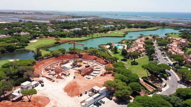 Aerial view of luxury construction site in Vale do Lobo, Portugal, with circular foundation, golf course, villas, lagoons and ocean in background. Concept of premium coastal infrastructure development