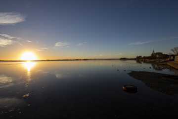 View of the gleaming sun kissing the water's surface, casting a radiant glow across the still lake in Christchurch, Canterbury Region, New Zealand.