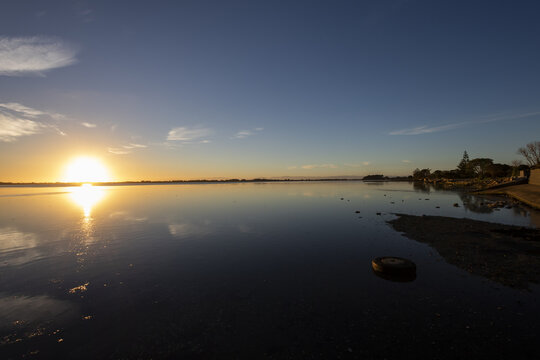 View of the gleaming sun kissing the water's surface, casting a radiant glow across the still lake in Christchurch, Canterbury Region, New Zealand.