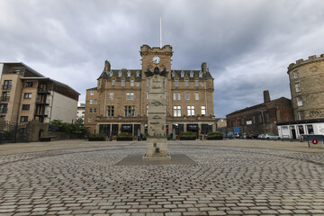 Edinburgh, United Kingdom - 23 June 2016: View of a stone monument standing tall on cobblestones before the historic Balmoral hotel, under a heavy, brooding sky.