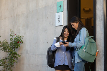 Young diverse students standing on campus, sharing content on a smartphone, connecting through social media apps, discussing school work and enjoying friendship moments