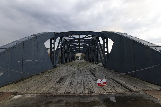 View of a long, blue steel bridge with old wooden planks stretches towards the horizon under a cloudy sky, its intricate metalwork casting shadows, Edinburgh, Scotland, United Kingdom.